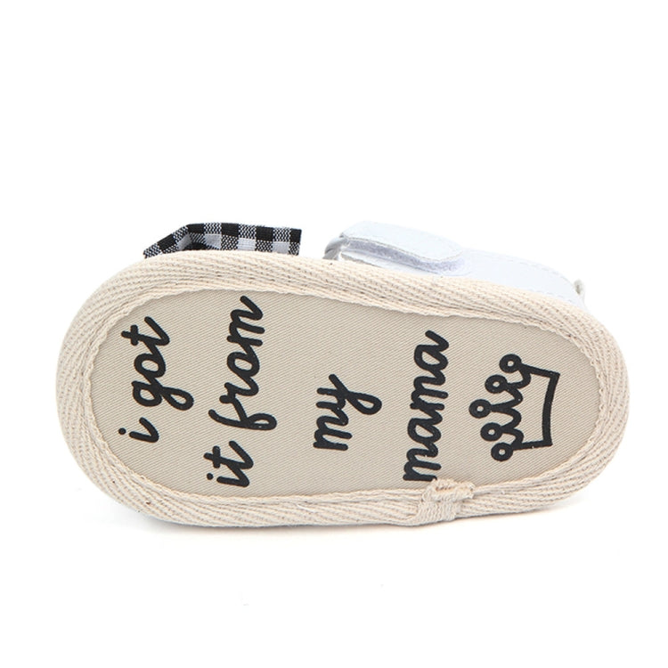 Baby sandal outsole close-up with dark plaid bow and printed lettering