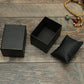 Black textured jewelry box open with inner tray and padded ring bag