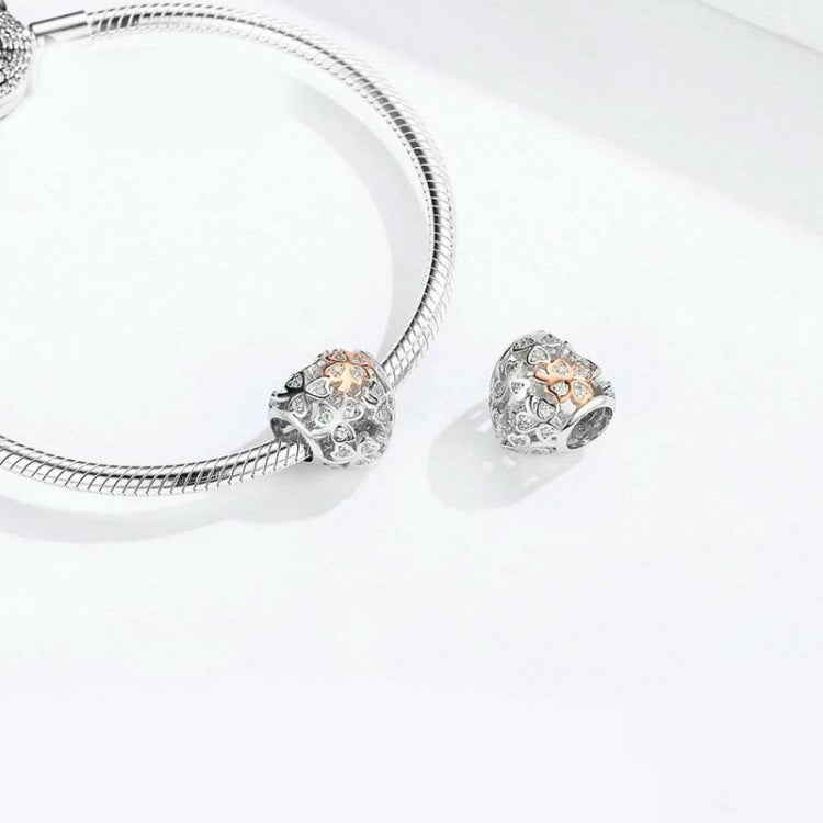 Heart-shaped charm bead beside a silver snake bracelet clasp; rose gold clover center visible.