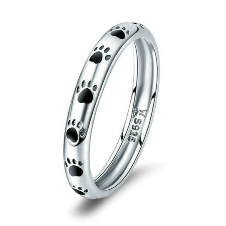Sterling silver paw print ring with black enamel footprints, angled studio view