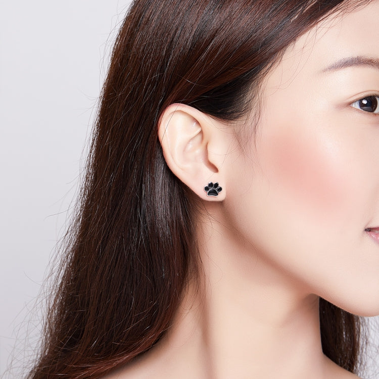 Black enamel paw print stud earring on sterling silver, worn on ear