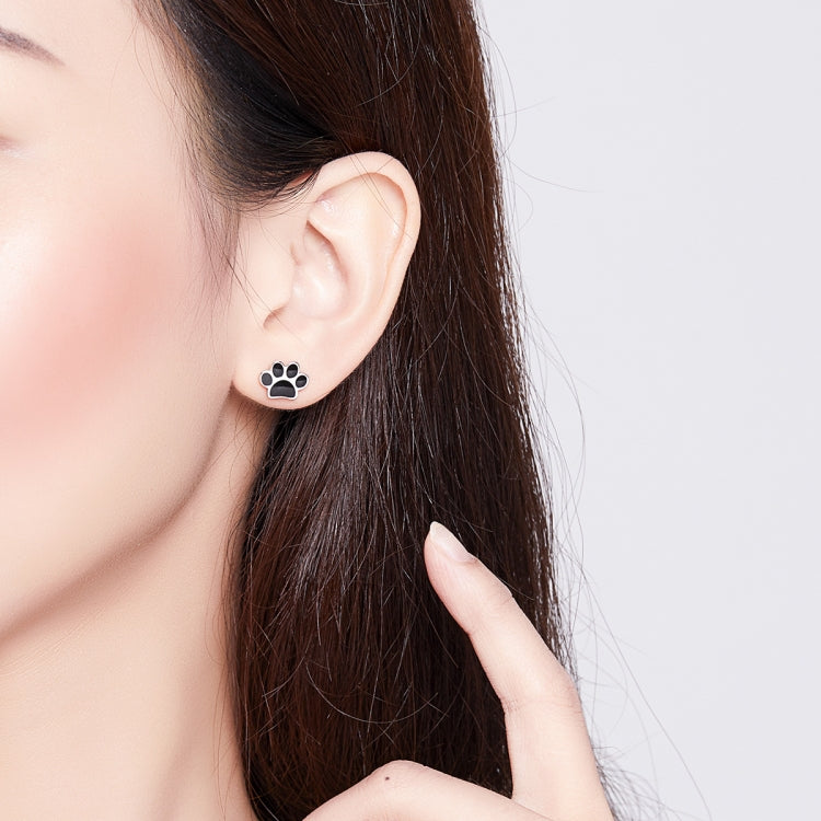 Sterling silver paw print stud earring with black enamel pads, side view on ear