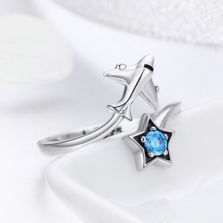 Silver open ring with airplane and star charm, featuring a blue center gem