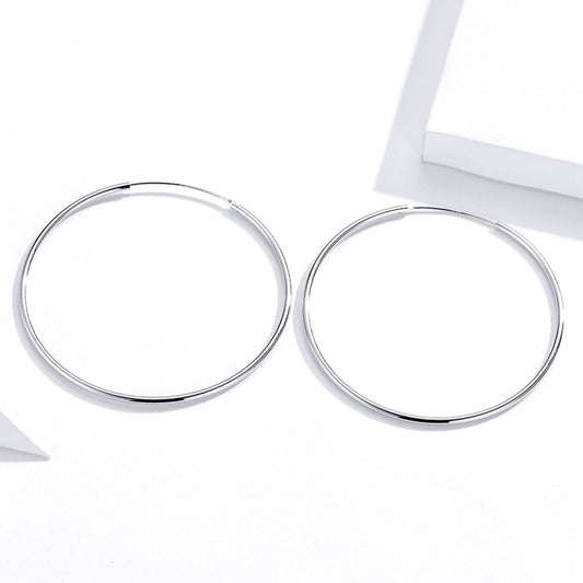 Silver-tone large oval hoop earrings with hinged clasp, angled view