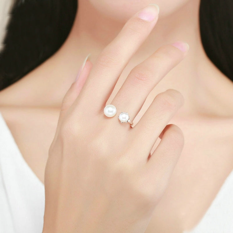 Open sterling silver ring with two round white pearl-style stones on finger