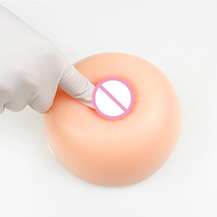 Round silicone breast insert with artificial areola, held in gloved hand