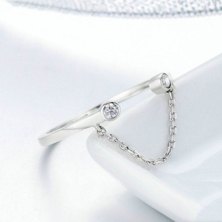 Close-up of silver open ring with round CZ stone, chain across band, prong setting