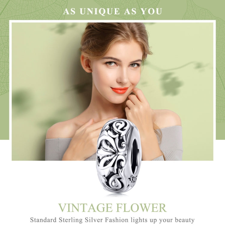 Sterling silver flower-pattern bead charm held near neckline, oxidized swirl details