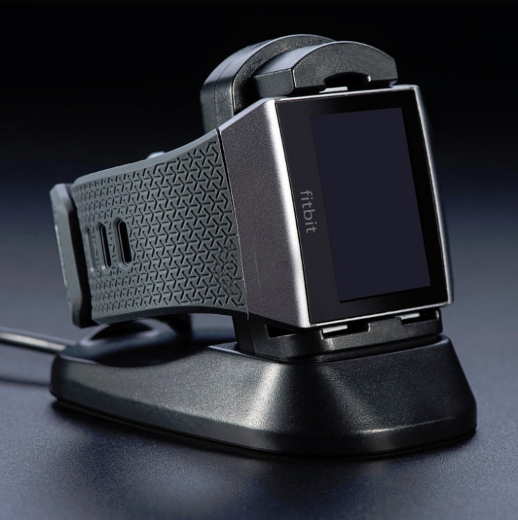 Black Fitbit smartwatch charging dock with seated watch and contact pins