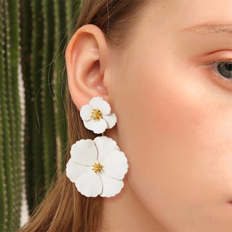 White flower earrings close-up: small stud and larger dangling flower with gold-tone center