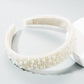 White pearl headband with beige inner band on a display, wide decorative crown.