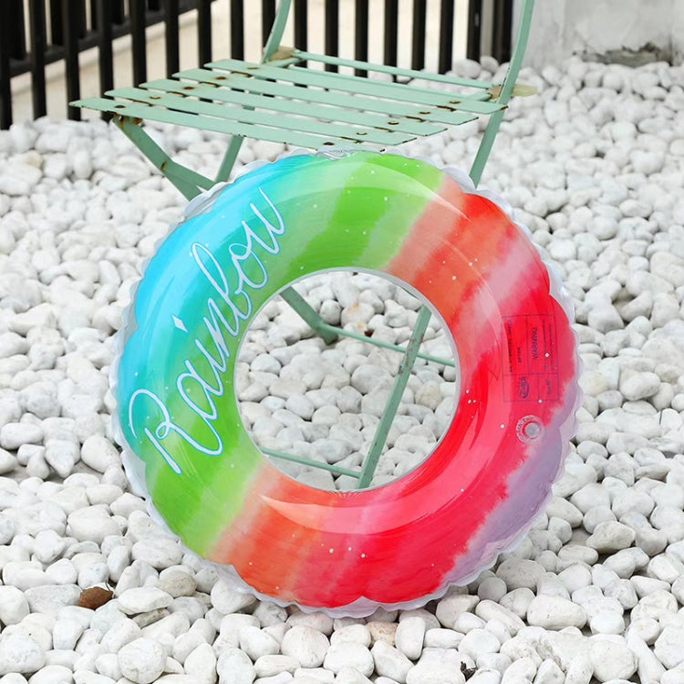 Rainbow gradient swimming ring resting on white pebbles, “Rainbow” script visible