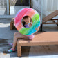Child sitting on pool bench wearing a rainbow gradient PVC swimming ring