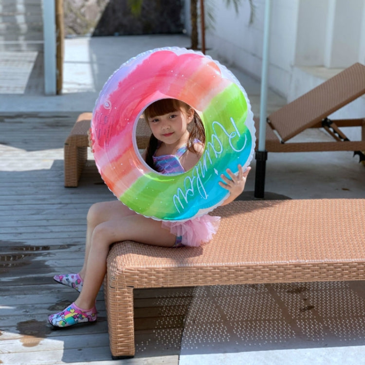 Child sitting on pool bench wearing a rainbow gradient PVC swimming ring
