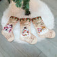 Set of three beige Christmas stockings with Merry Christmas and winter character prints.