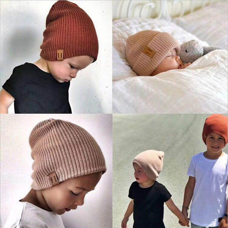 Tan knit baby beanie with folded cuff and square leather patch, worn on child