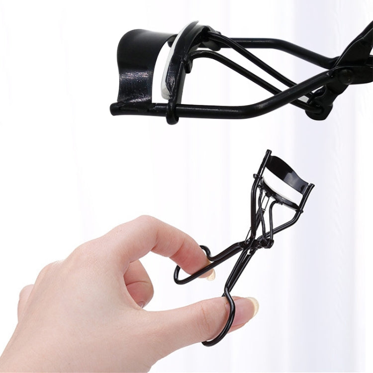 Black eyelash curler clip held in fingers, with light metallic pad and curved frame.