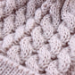 Cream knit beanie fabric close-up with raised cable pattern and cozy ribbed brim