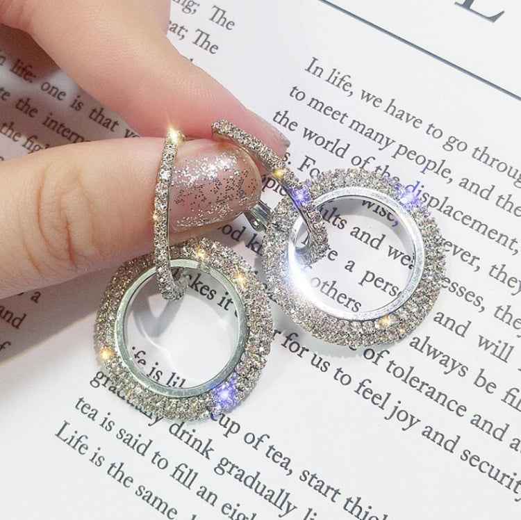 Silver-tone round rhinestone hoop earrings with small top ring, held by fingers