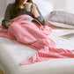 Knitted mermaid tail blanket in pink, wrapped around legs with fin tail visible