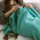 Knitted mermaid tail blanket in teal, pulled up around shoulders and legs