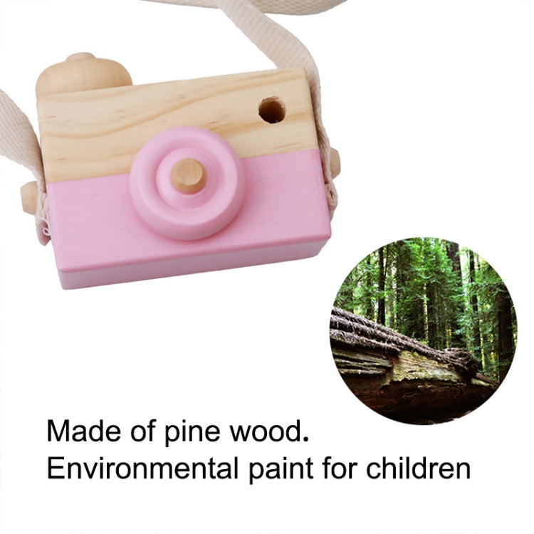 Children's wooden camera toy with pink body, round lens, and cloth strap