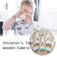 Children's wooden camera toy held by a child, with pink round lens and fabric strap