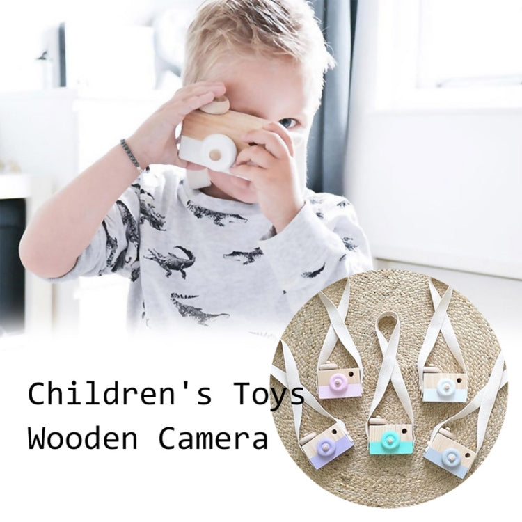 Children's wooden camera toy held by a child, with pink round lens and fabric strap