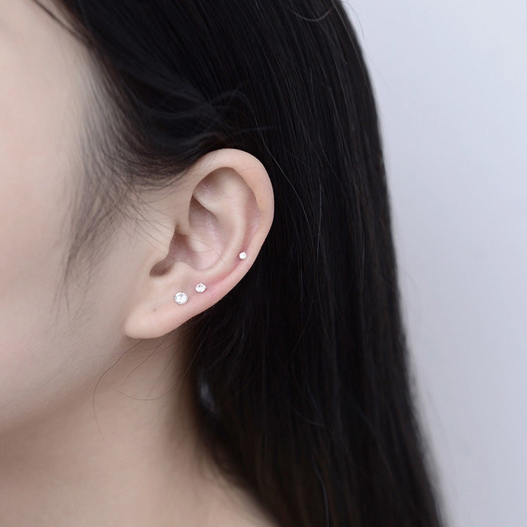 Ear with three small zircon stud earrings lined up, clear stones