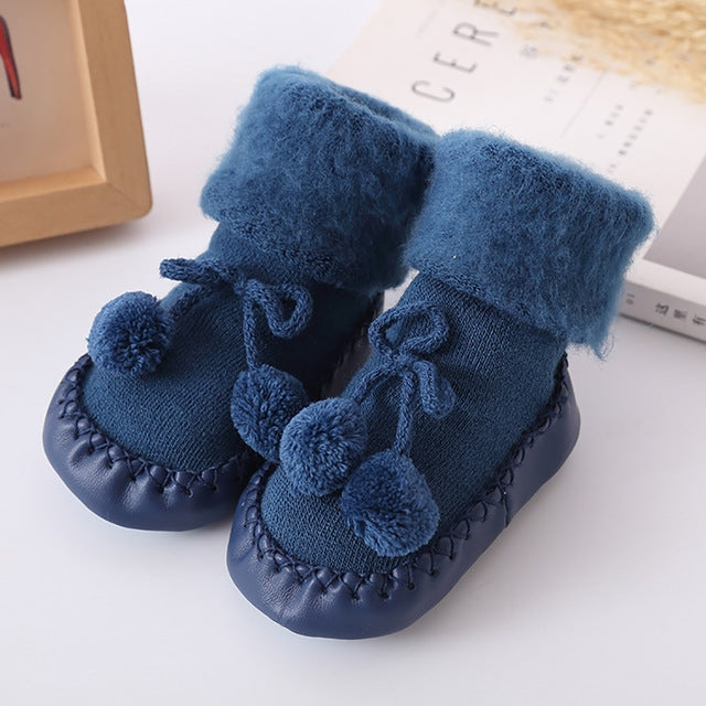 Blue plush baby floor socks with pom-pom accents and tie bows