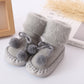 Gray plush baby floor socks with pom-pom accents and stitched non-slip soles