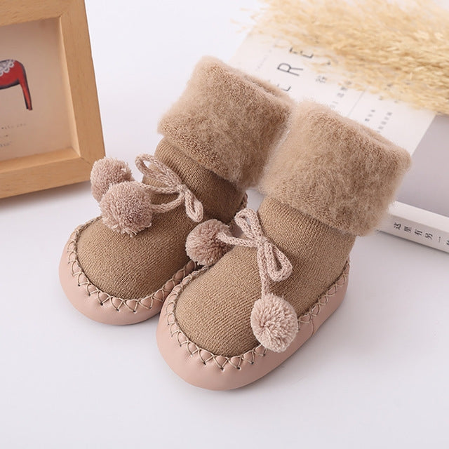 Tan plush baby floor socks with pom-pom accents and tie bows