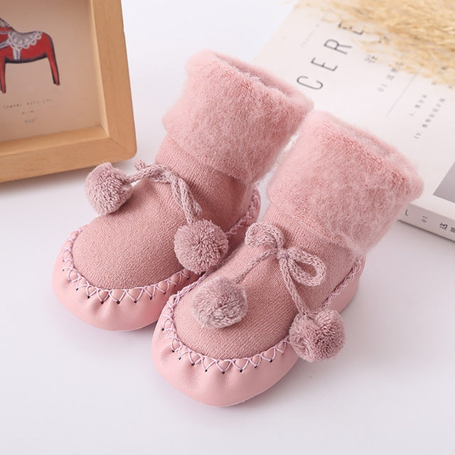 Light pink plush baby floor socks with pom-pom accents and bow ties