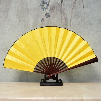 Yellow blank silk folding fan with dark red center and scalloped radial border on a stand.