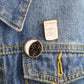 Enamel brooch pins on denim: round moon constellation and “Good Vibes” bottle pin.