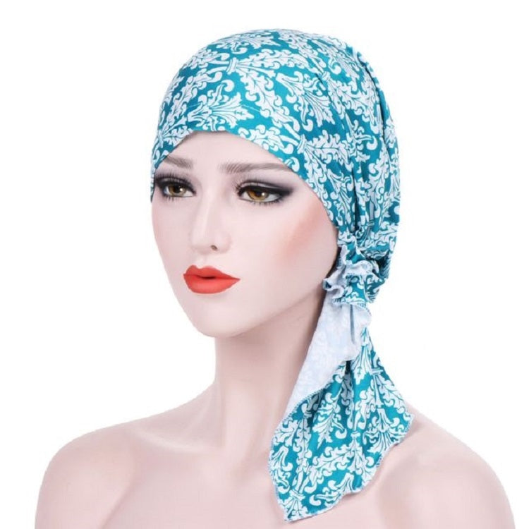 Stretch printed turban hat with long side tail, teal and white ornate pattern