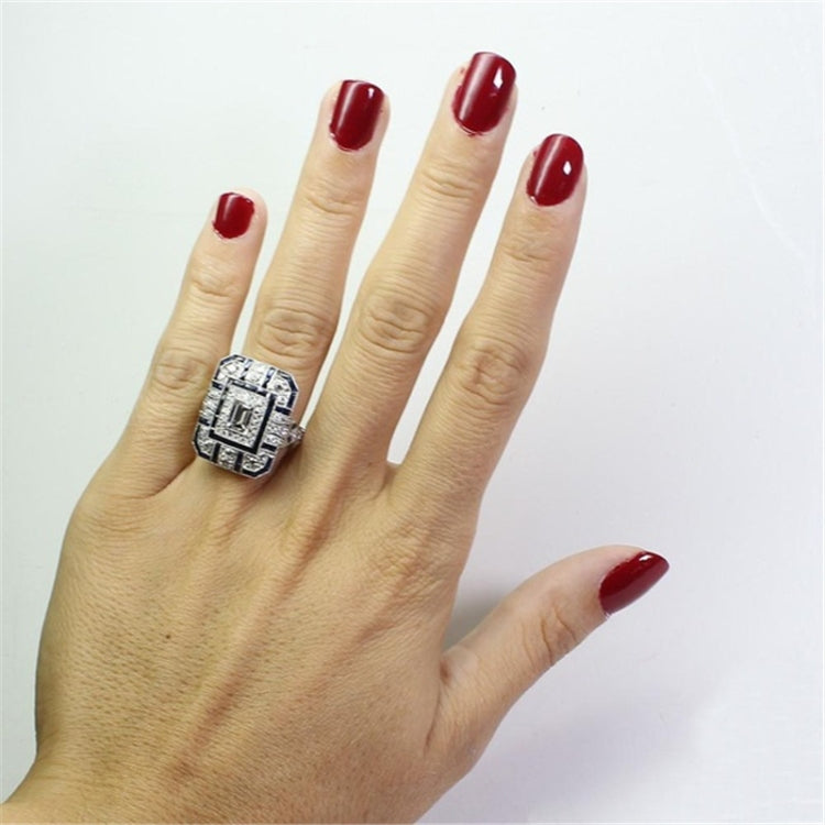 Square-cut crystal halo ring on finger with dark red nails and dark blue accents