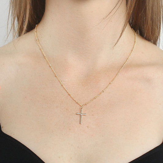 Gold cross pendant necklace on a woman’s neckline with fine chain link style.