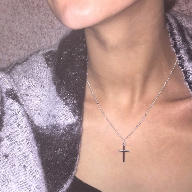 Silver cross pendant necklace on a woman’s neckline with a slim linked chain and cross charm.