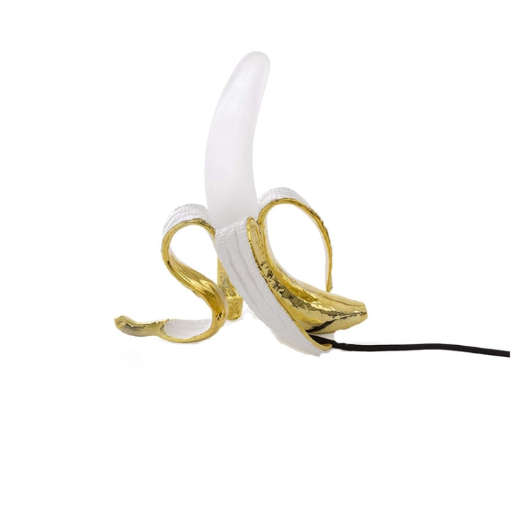 Banana table lamp with gold banana body, white bulb, and black power cord