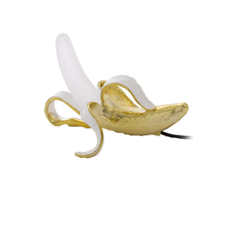 Banana table lamp with gold banana body, white bulb, and black power cord