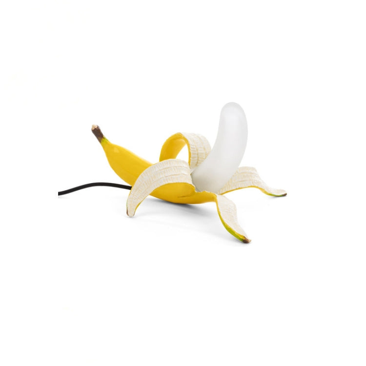 Banana-shaped table lamp with yellow banana body and white bulb, lying pose