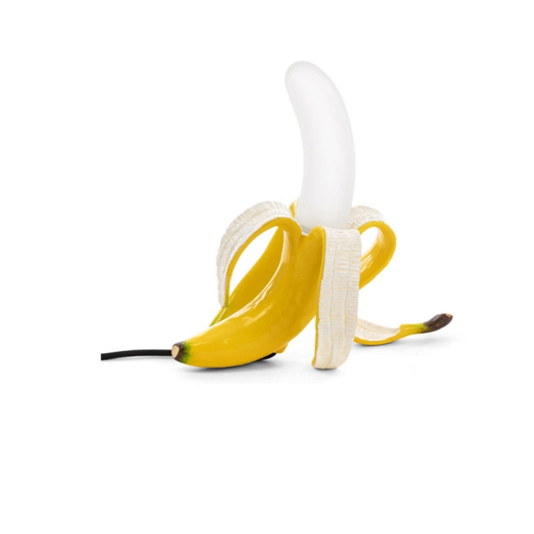 Banana-shaped table lamp with yellow banana body and white bulb, sideways pose