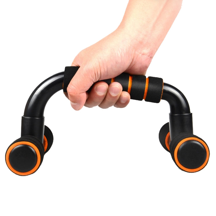 Hand holding a black H-shaped push-up bracket with orange foam grip pads