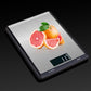 Stainless steel kitchen digital scale with fruit on top and green-lit digital display