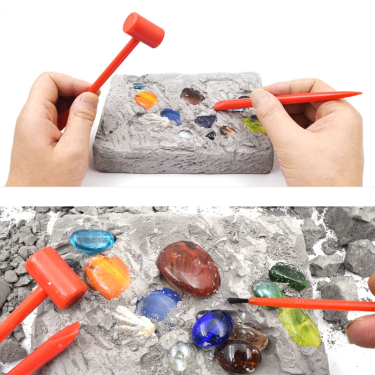 Hands holding orange digging tools over gray gem excavation rock with colorful gems