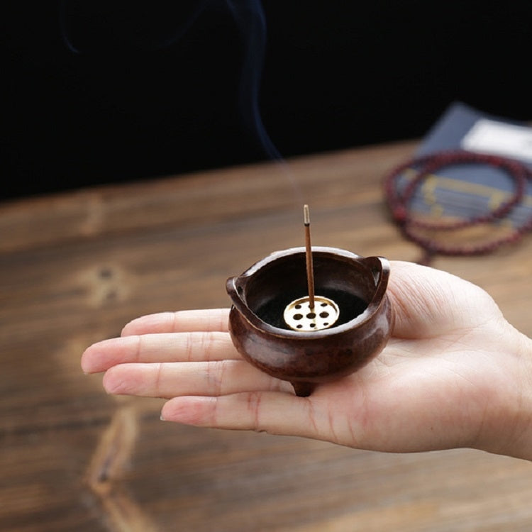 Small copper incense burner held in hand, with central stick and perforated insert
