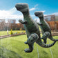 Two green inflatable dinosaur water-spray toys spraying with hoses in yard