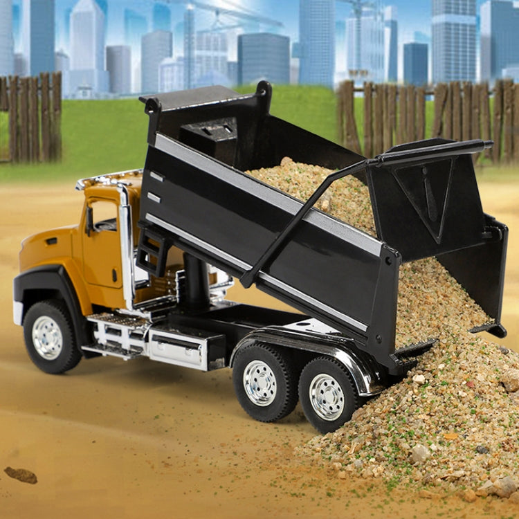 Die-cast dump truck toy tipping black bed over a gravel pile