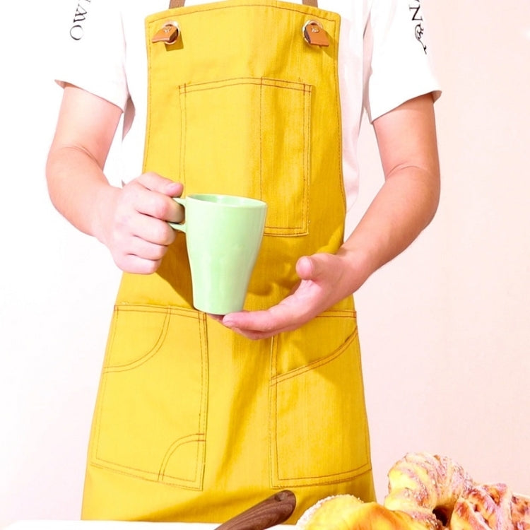 Yellow denim apron with front pockets and adjustable straps, worn holding a mug